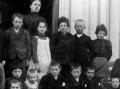 Et gammelt bilde av elever samlet til skole i Sk�lv�rg�rden i 1905 eller 1906. Det har ikke lykkes � finne ut hvem alle er, men det man kan si med en viss sikkerhet er at: Jentungen i med det hvite forkledet i bakerste rekke er Alma Edvardsdatter (Svendsen) fra Naut�en, datter til Josefine Ryan, s�ster til smeden, og Edvard Svendsen. Gutten med tverrsl�yfe i venstre bildekant er Thorvald Wiig, s�nn til Benedicte og Edvin O. Wiig, som overtok handelsstedet etter R�ringene. De tre gutten midt p� trappa er s�nner til Elen og Johan Agersborg, Det er ikke mulig med sikkerhet � si hvem er hvem, men de fire mest aktuelle er Peter, Toralv,  Ole og �yvind. Bildet er tatt ved hovedinngange i Sk�lv�rg�rden, og viser de skolebarna som soknet til Sk�lv�r. Det ble holdt skole b�de i G�rden, p� M�lnhushaugen og p� Hansihaugen. Bildet eies av Kari Sommerseth Jacobsen.